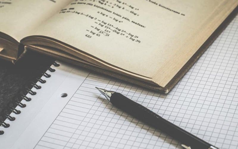 A notebook of worked Maths equations beside a pen